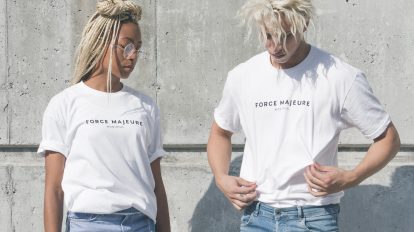 man and woman in white-and-gray force majeure-printed crew-neck t-shirts standing near gray concrete wall
